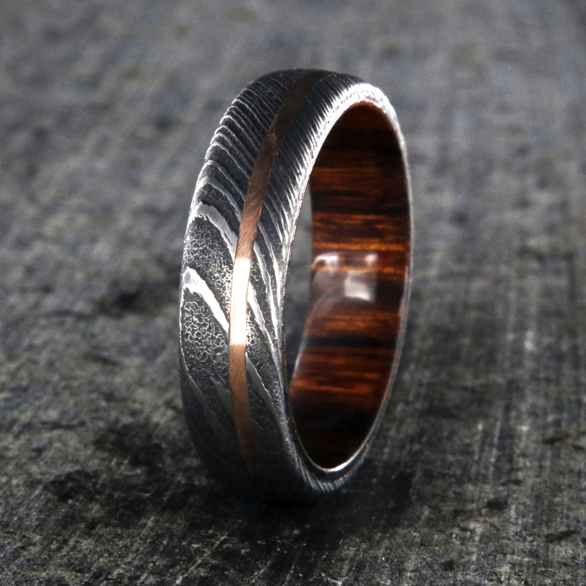6mm wide black Damascus steel ring with off-center rose gold inlay and an Arizona ironwood sleeve