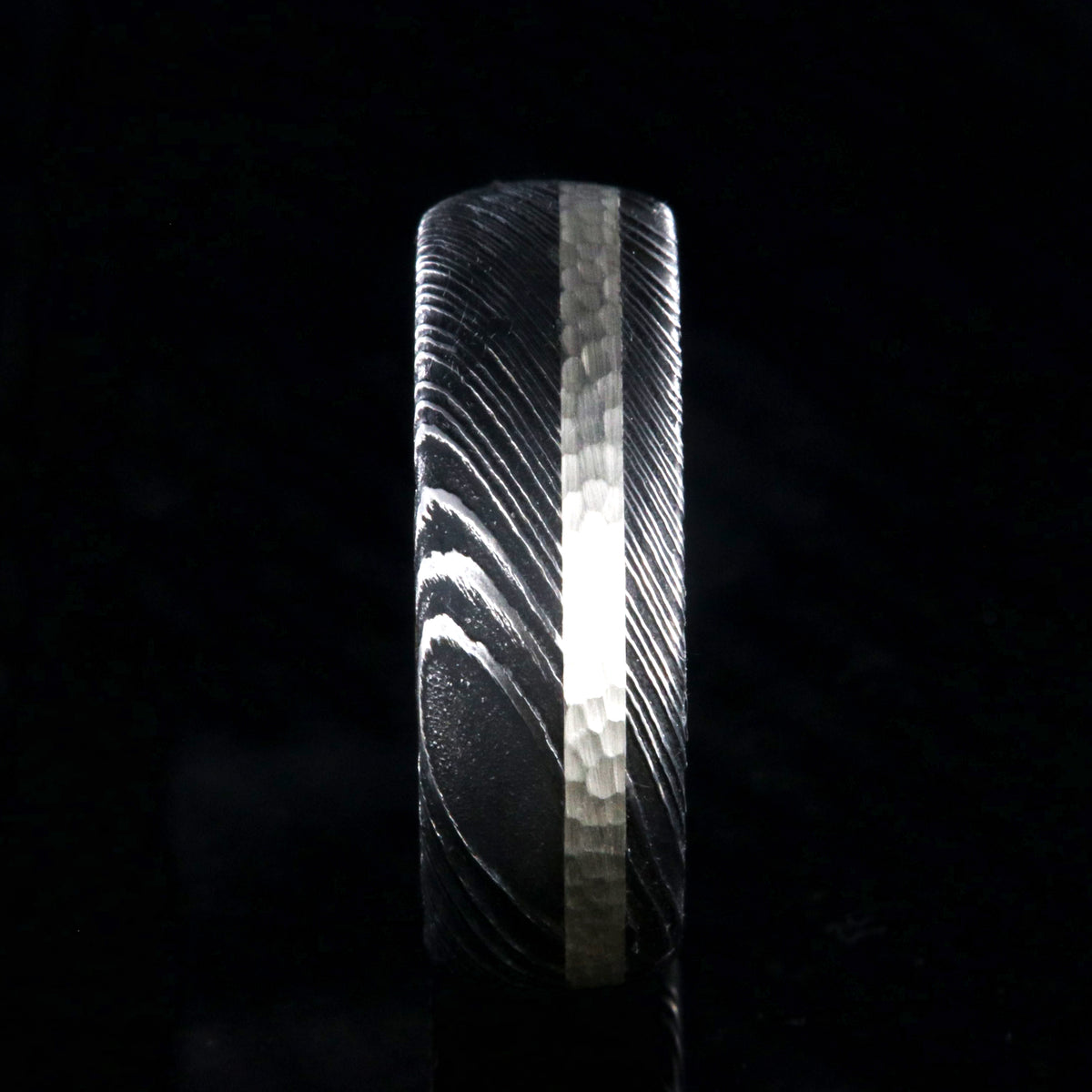 8mm wide black Damascus steel wedding band with a hammered 2mm wide sterling silver inlay and a whiskey barrel sleeve