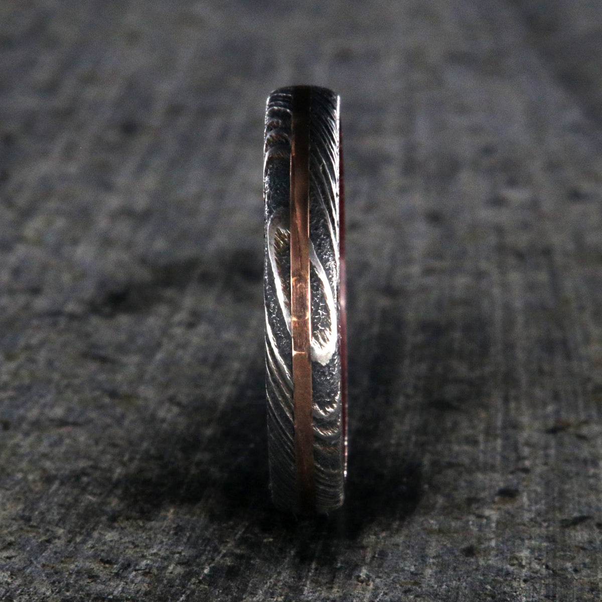 4mm wide women&#39;s wedding band made with black Damascus steel with a centered rose gold inlay and purple rain wood sleeve