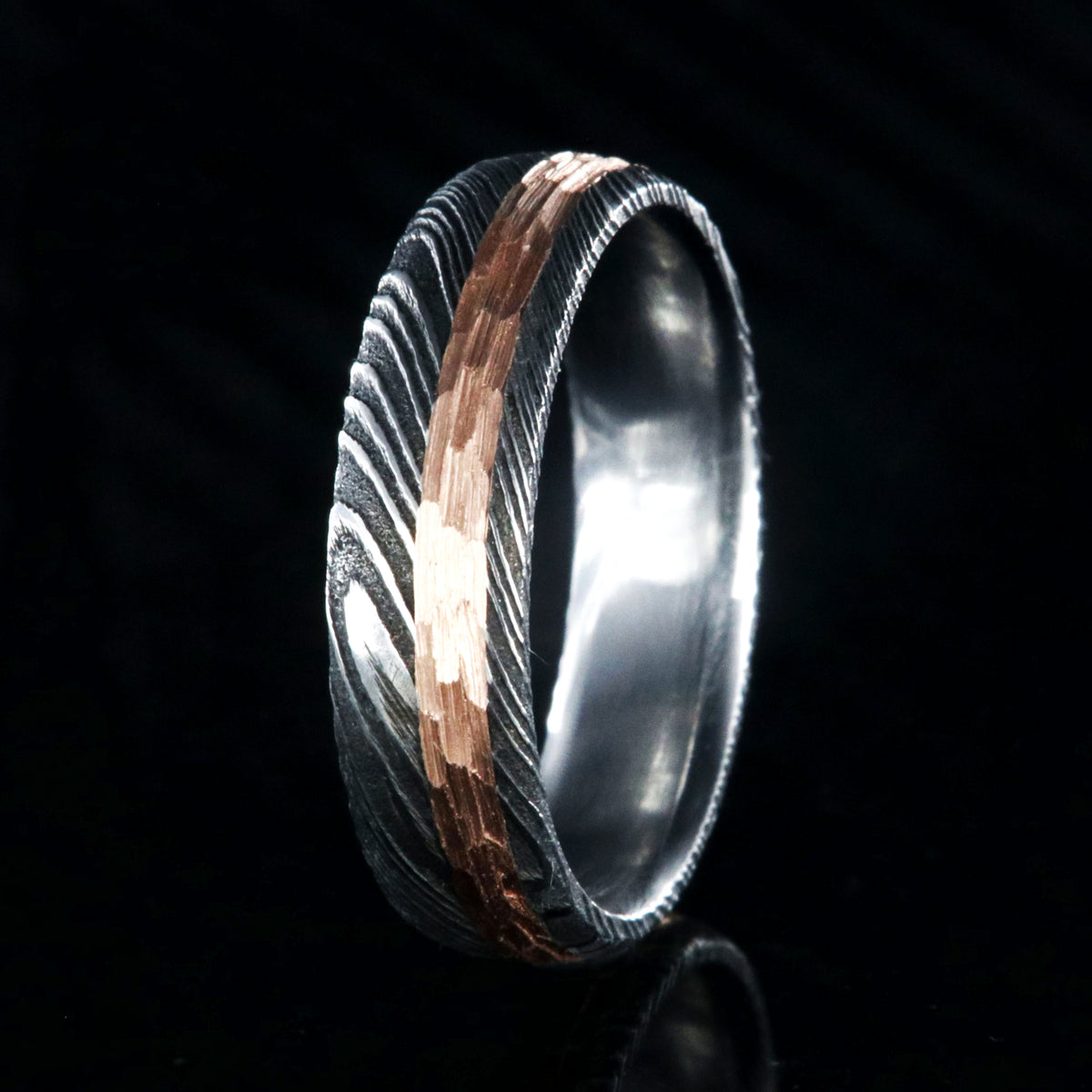 6mm wide black Damascus steel wedding band with a 2mm wide hammered rose gold inlay