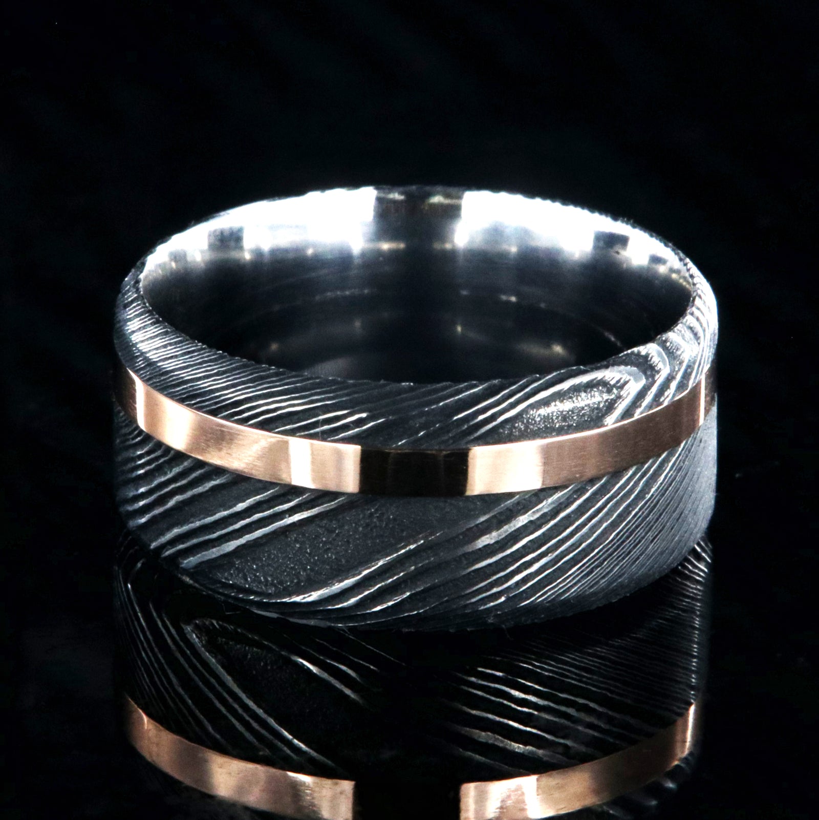 10mm wide black Damascus steel wedding band with an off-centered rose gold inlay and flat profile