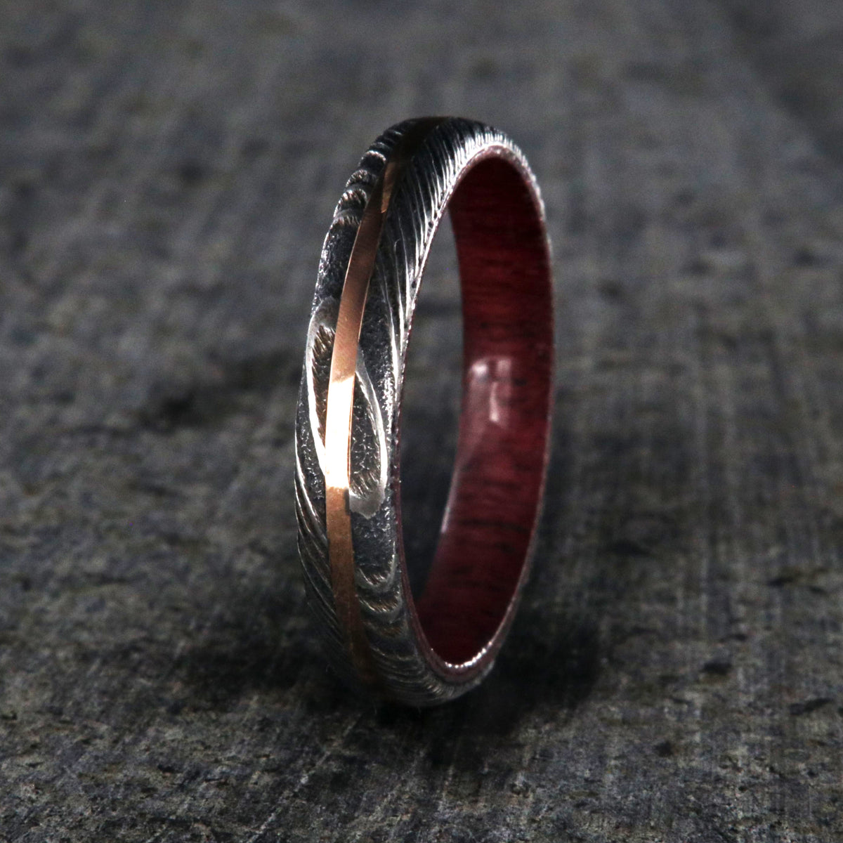 4mm wide women&#39;s wedding band made with black Damascus steel with a centered rose gold inlay and purple rain wood sleeve