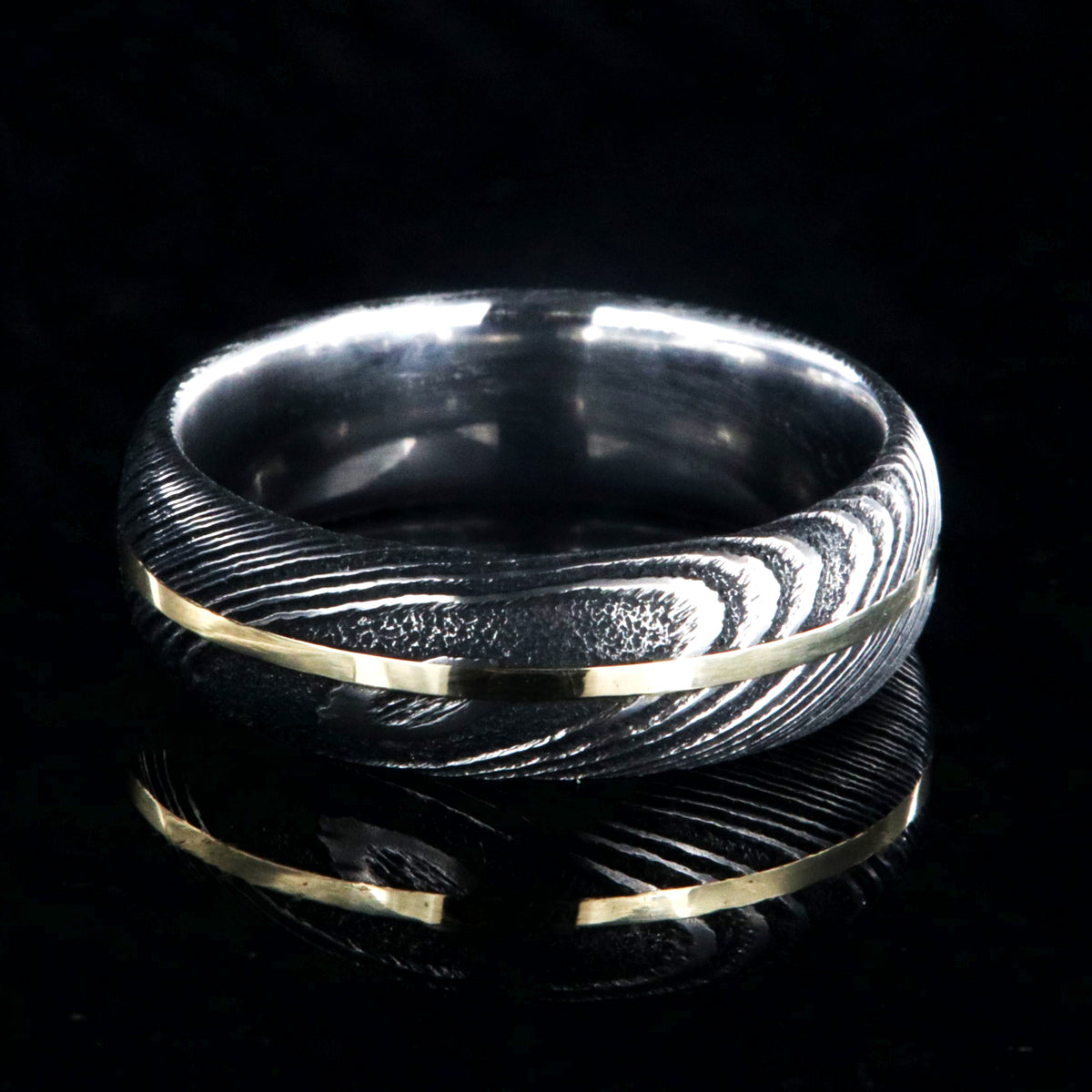7mm wide black Damascus steel wedding band with a centered yellow gold inlay and a rounded profile
