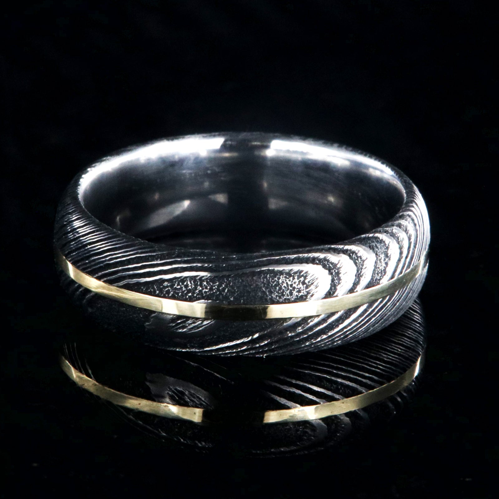 7mm wide black Damascus steel wedding band with a centered yellow gold inlay and a rounded profile