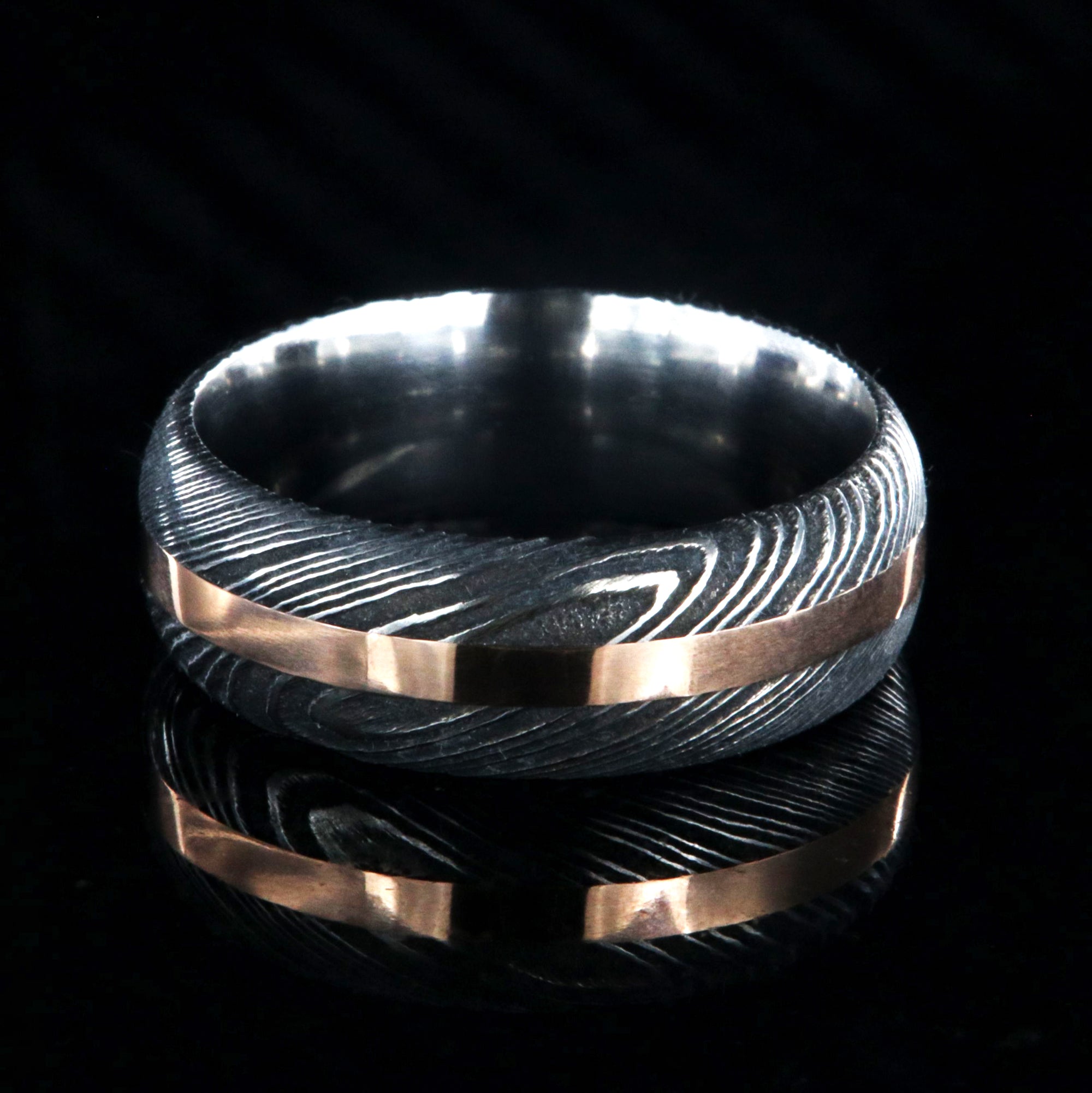 8mm wide black Damascus steel wedding band with a centered rose gold inlay and rounded profile