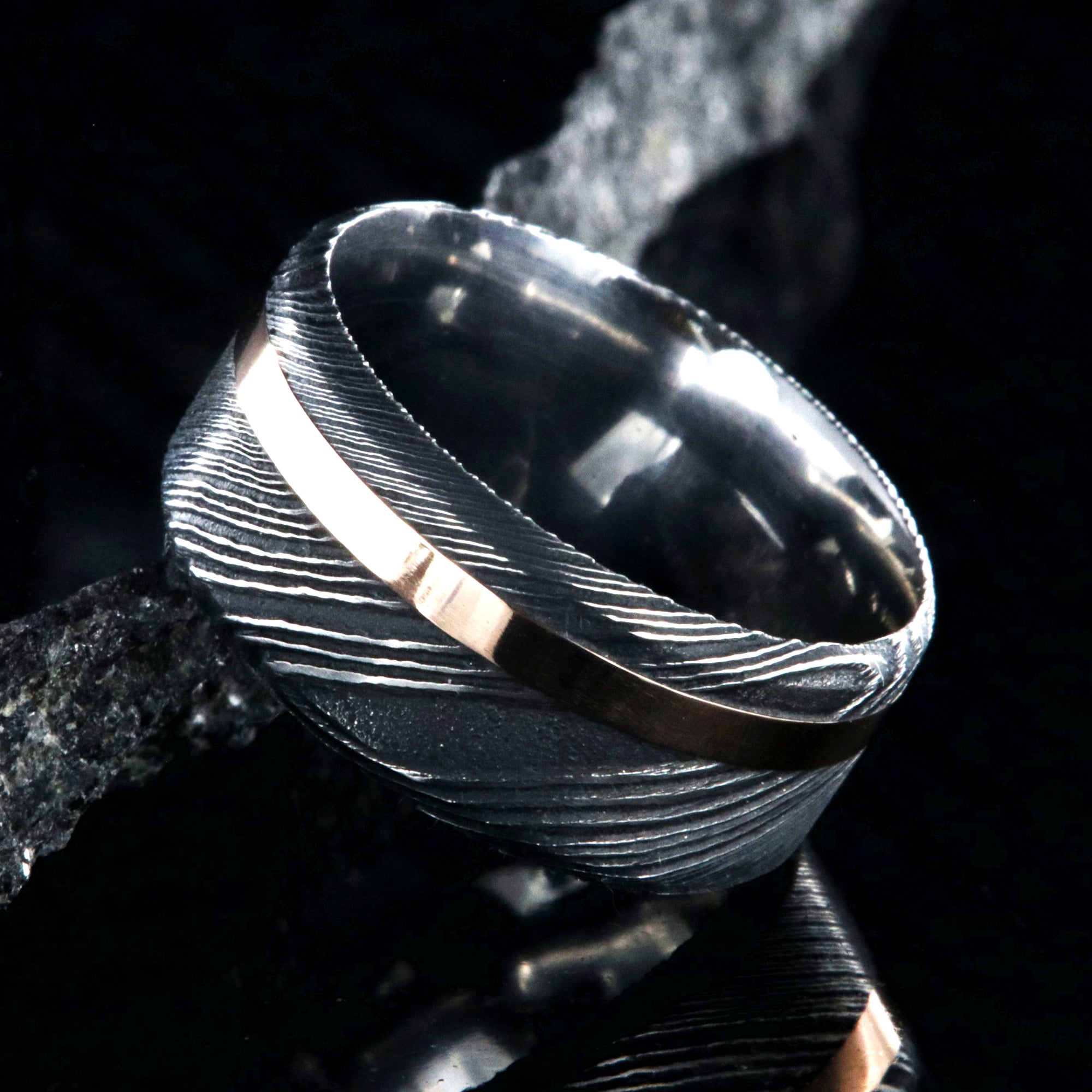 10mm wide black Damascus steel wedding band with an off-centered rose gold inlay and flat profile