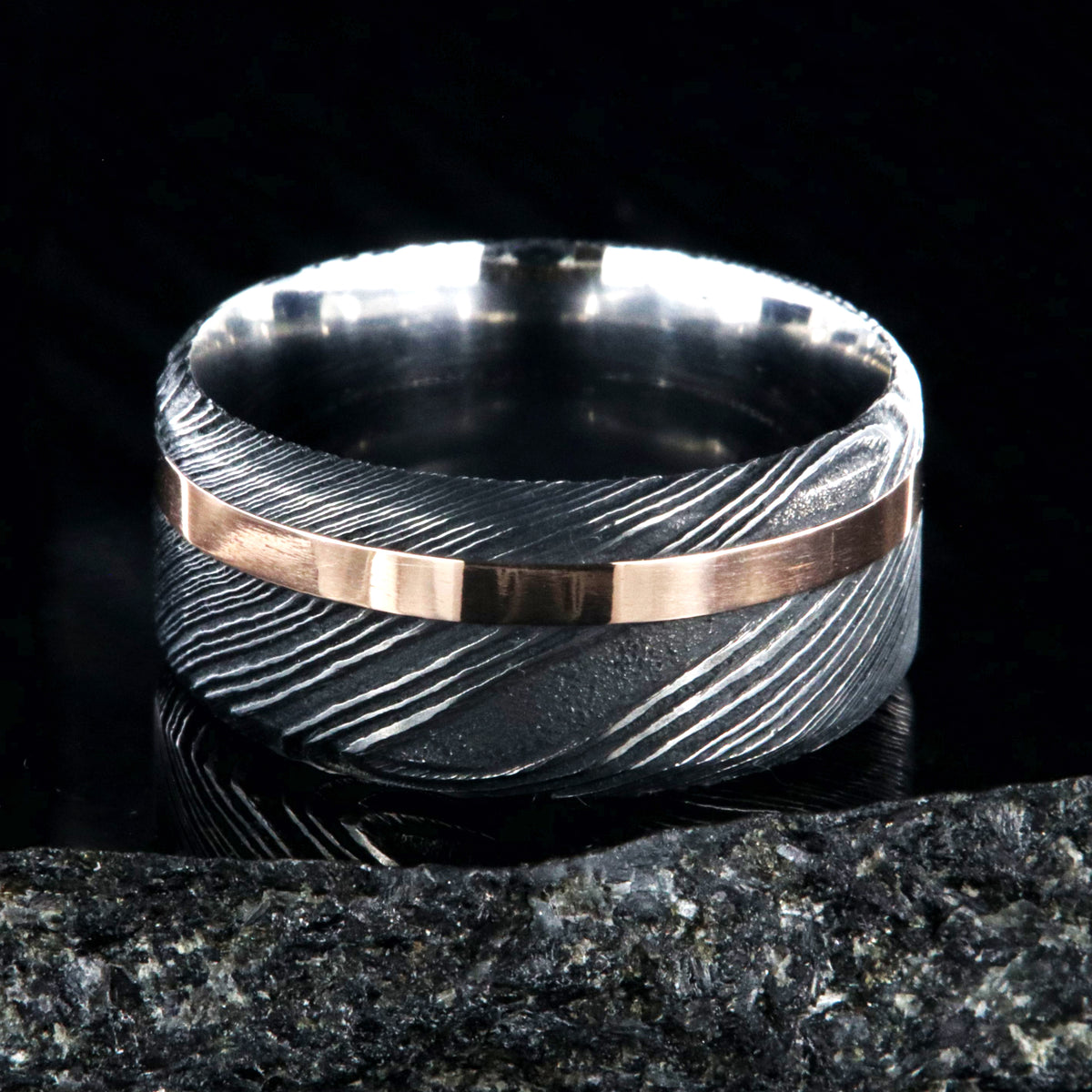 10mm wide black Damascus steel wedding band with an off-centered rose gold inlay and flat profile