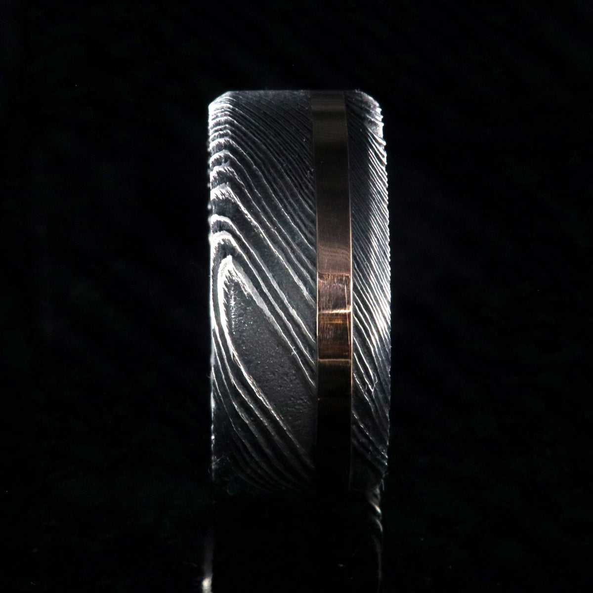 10mm wide black Damascus steel wedding band with an off-centered rose gold inlay and flat profile