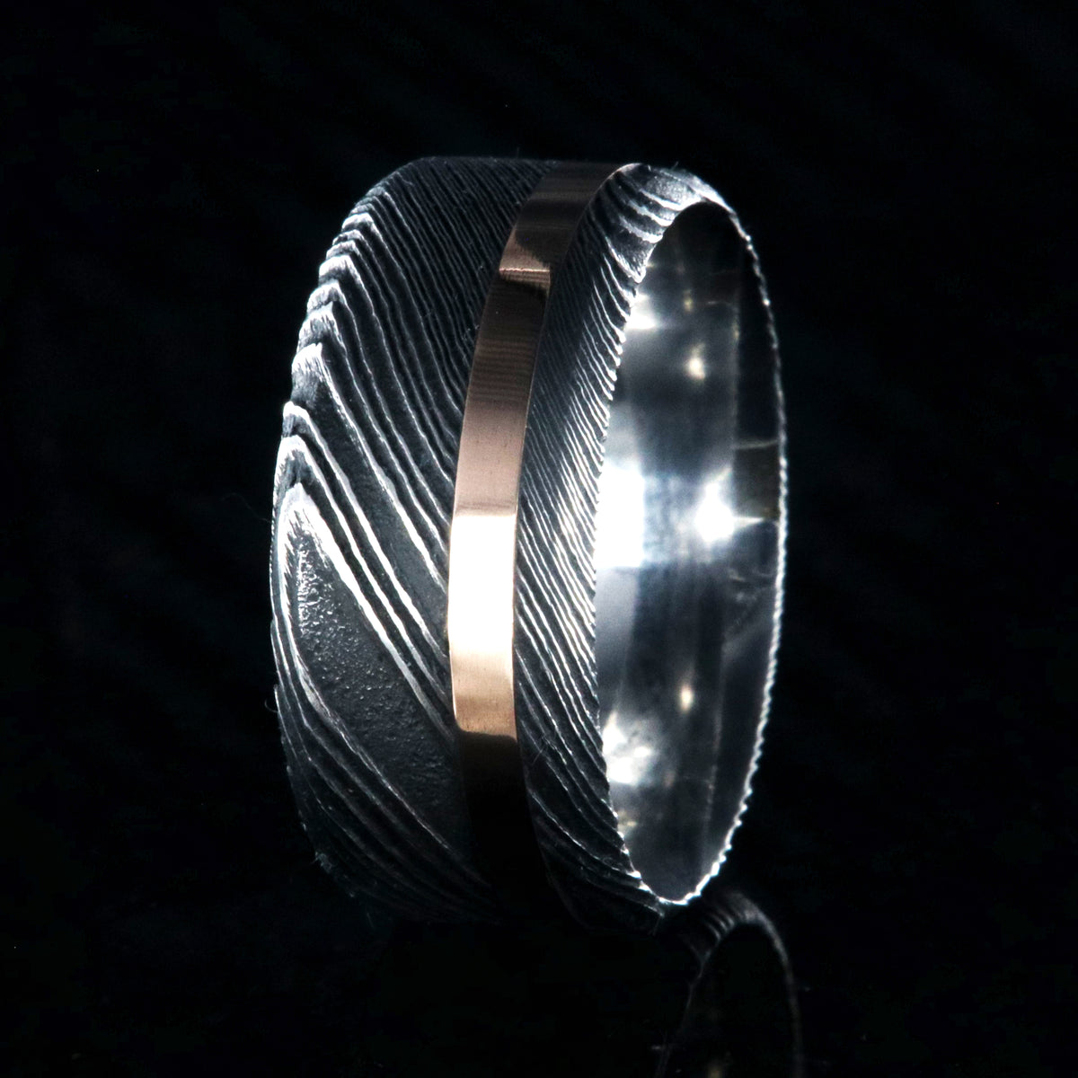 10mm wide black Damascus steel wedding band with an off-centered rose gold inlay and flat profile