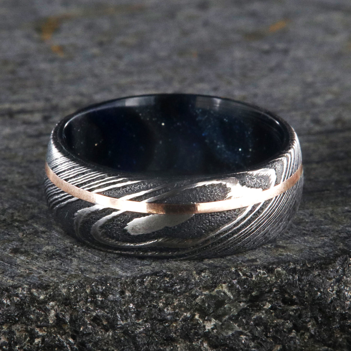 8mm wide Damascus steel wedding band with a thin rose gold off-center inlay and glittering blue and silver sleeve