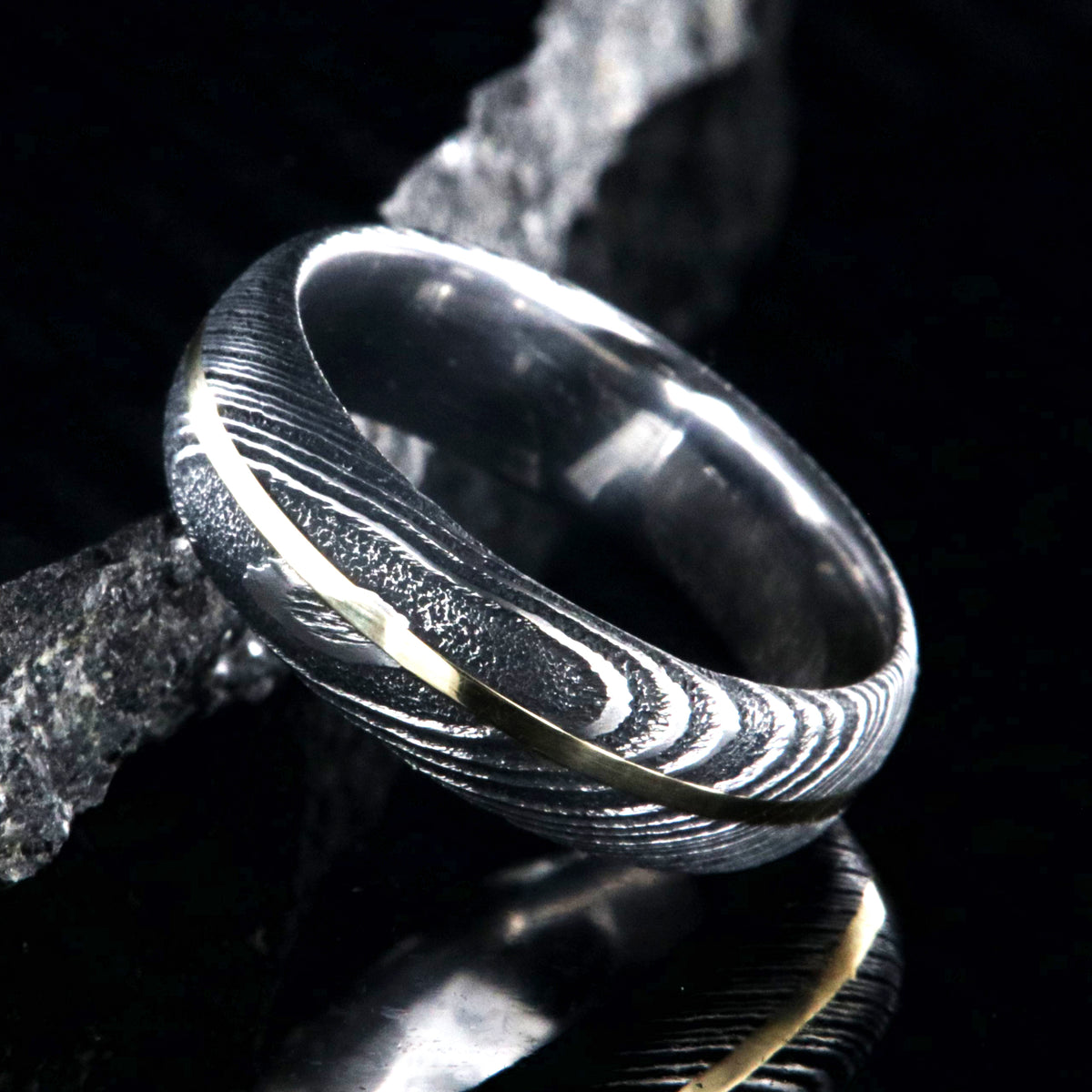 7mm wide black Damascus steel wedding band with a centered yellow gold inlay and a rounded profile