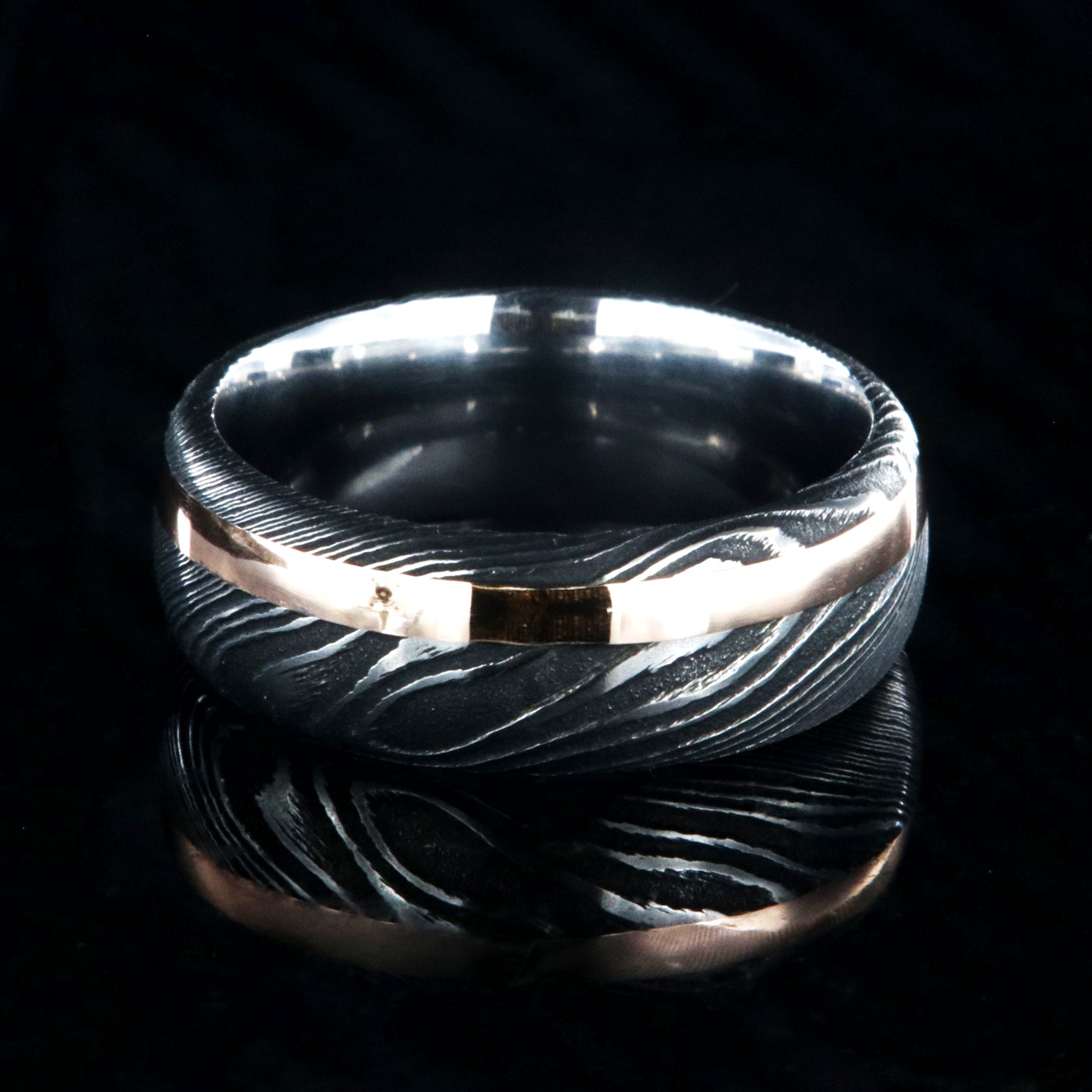 8mm wide black Damascus steel wedding band with a 2mm wide rose gold inlay and rounded profile