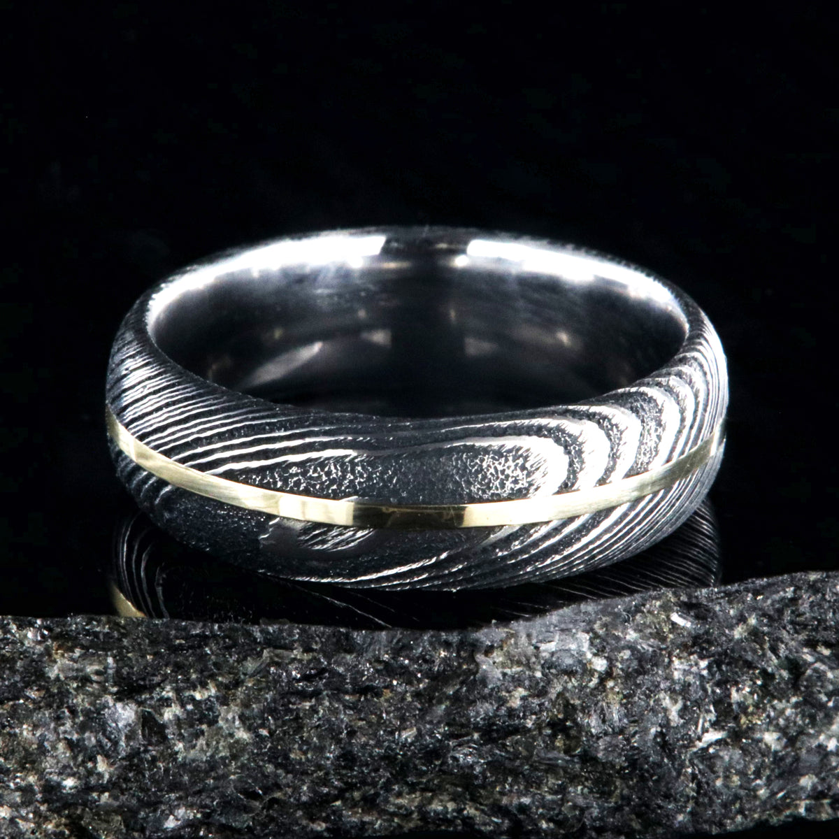 7mm wide black Damascus steel wedding band with a centered yellow gold inlay and a rounded profile
