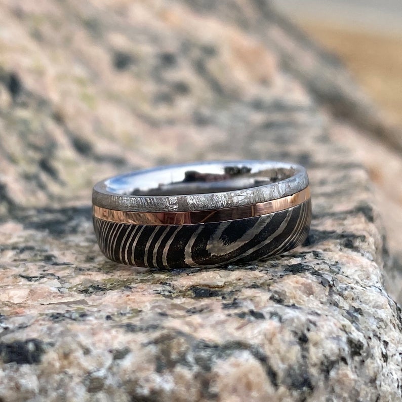 6mm wide men's wedding band with a wide edge of black Damascus, a center rose gold inlay, and thin meteorite edge