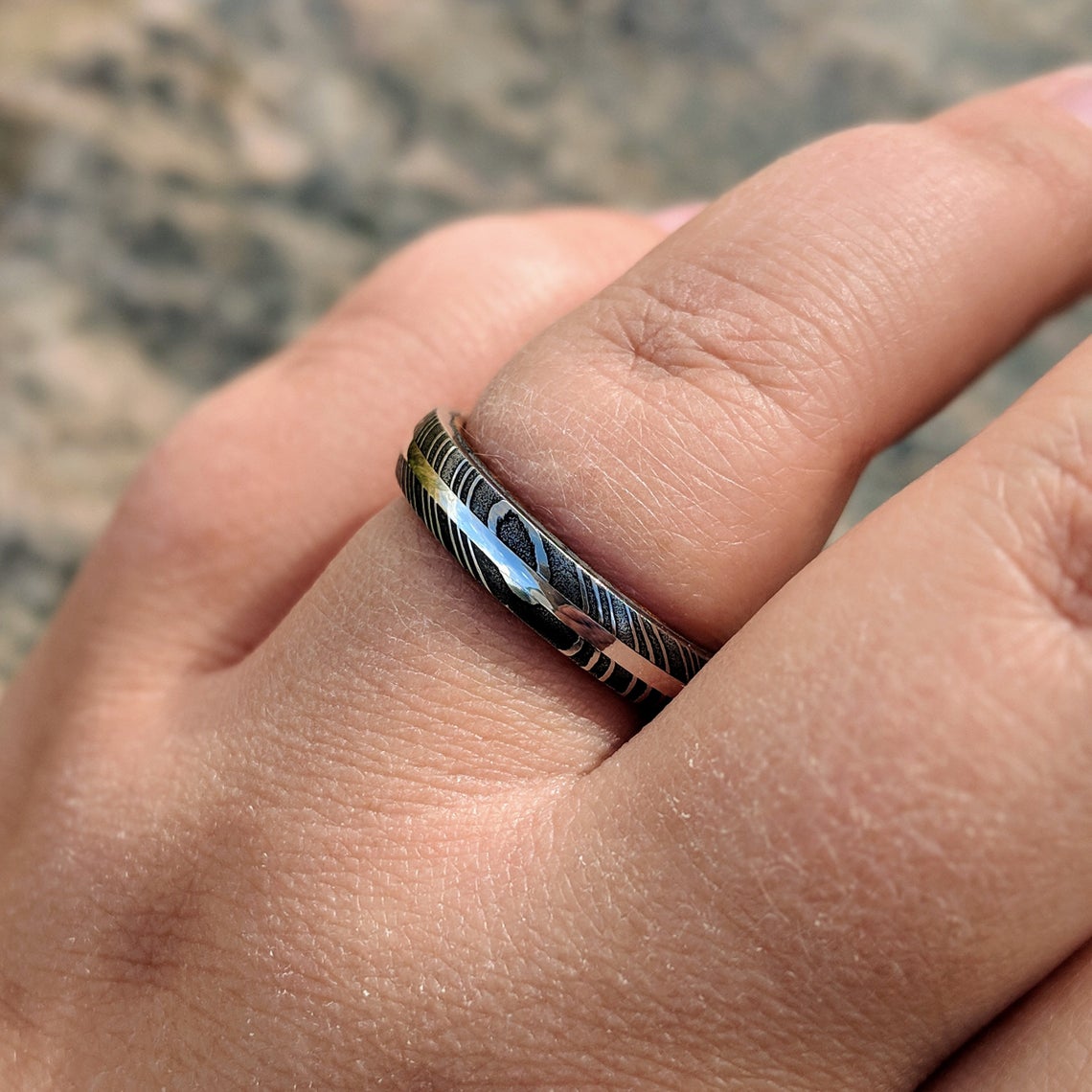 4mm wide black Damascus steel wedding band with a white gold inlay, Arizona ironwood sleeve, and a rounded profile on a woman&#39;s hand