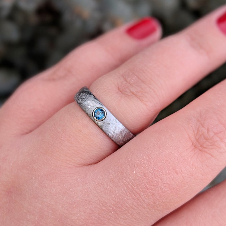 5mm wide women&#39;s meteorite ring with a blue topaz set in 14k gold bezel on woman&#39;s hand
