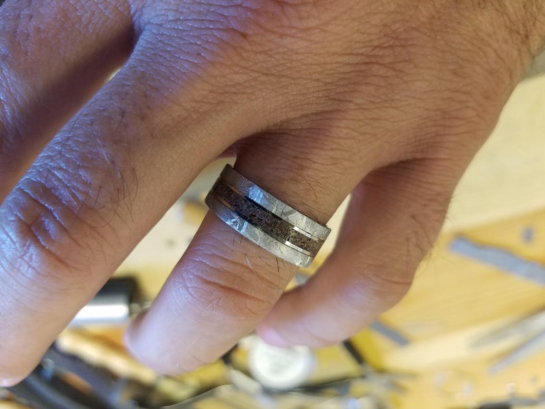 8mm wide Gibeon meteorite wedding ring for men with a dinosaur bone centered inlay with titanium sleeve on man&#39;s hand