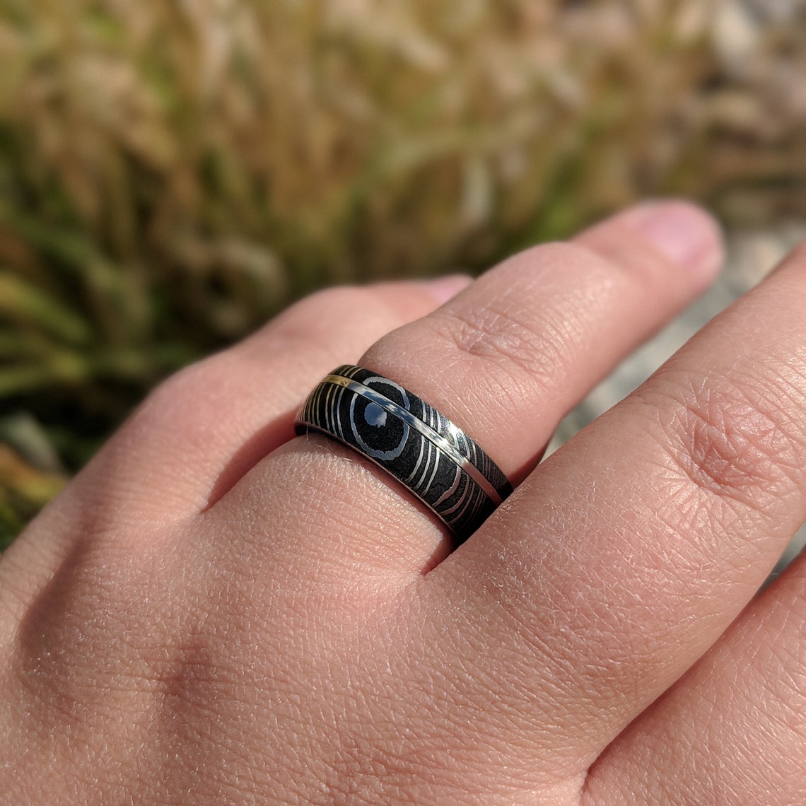 8mm wide black Damascus steel ring with a swirled blue acrylic sleeve and white gold inlay on hand