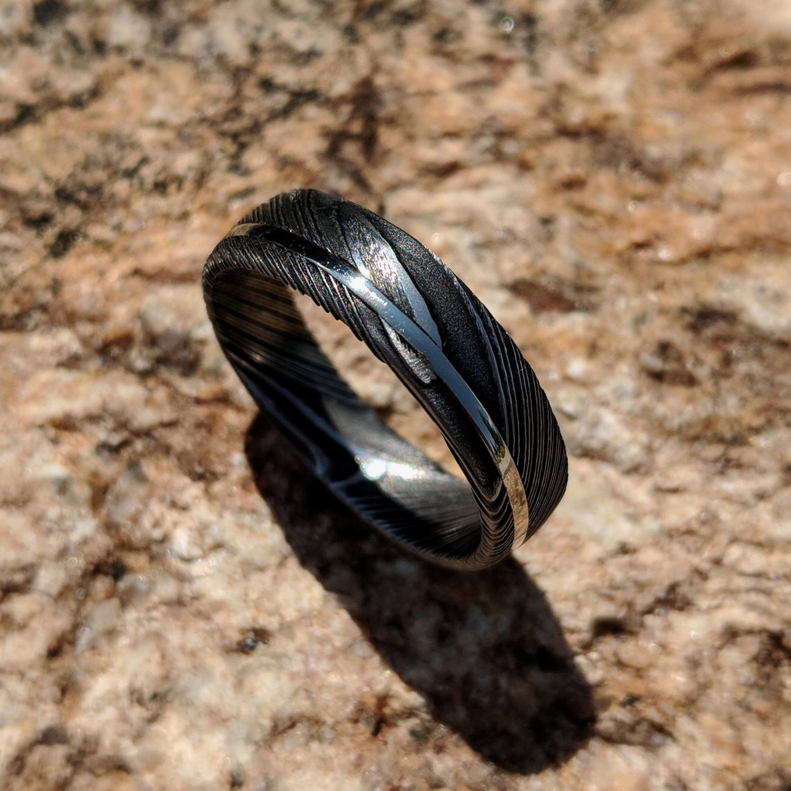 6mm wide black Damascus steel ring with an off-center white gold inlay