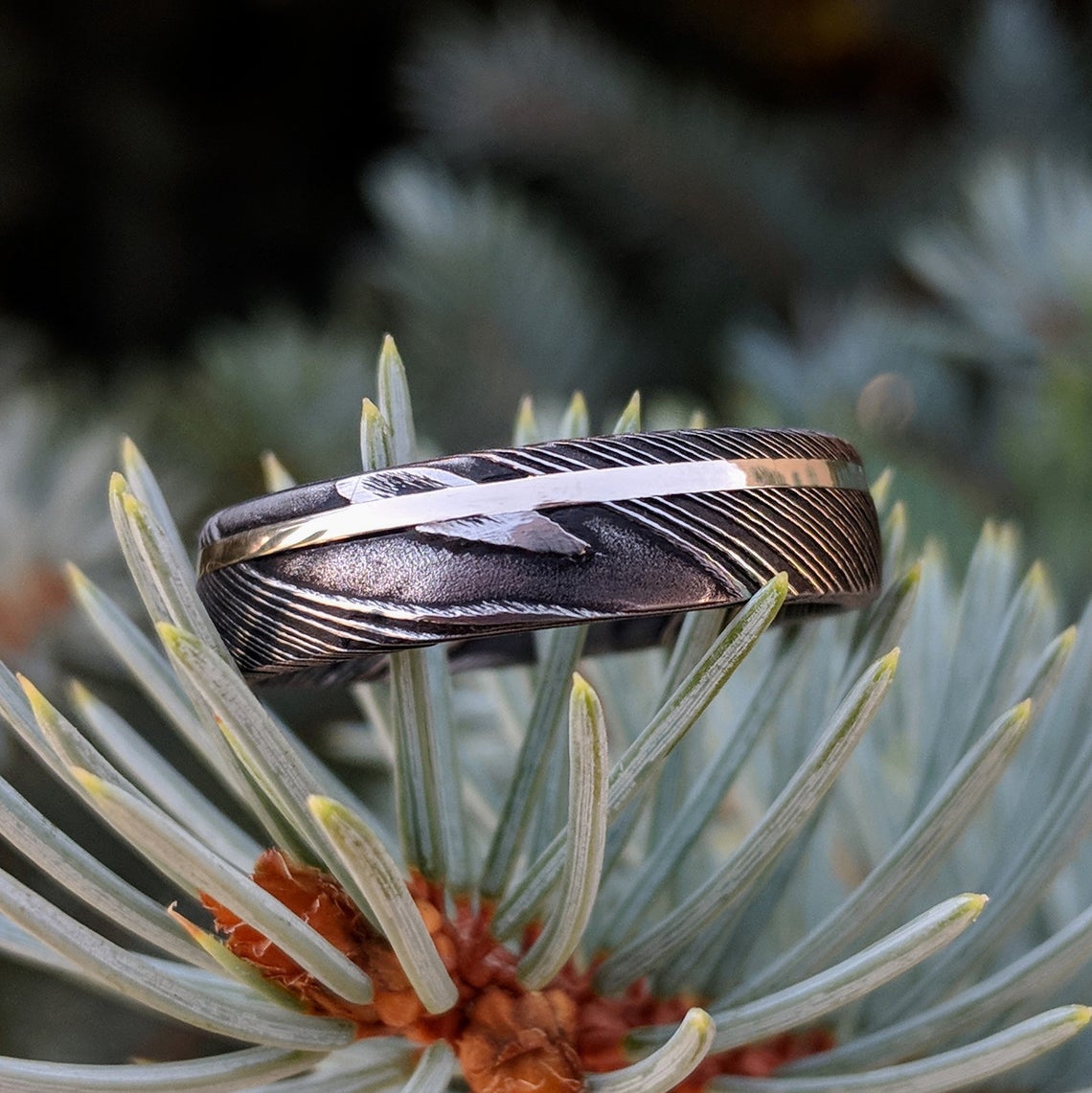 6mm wide black Damascus steel ring with an off-center white gold inlay