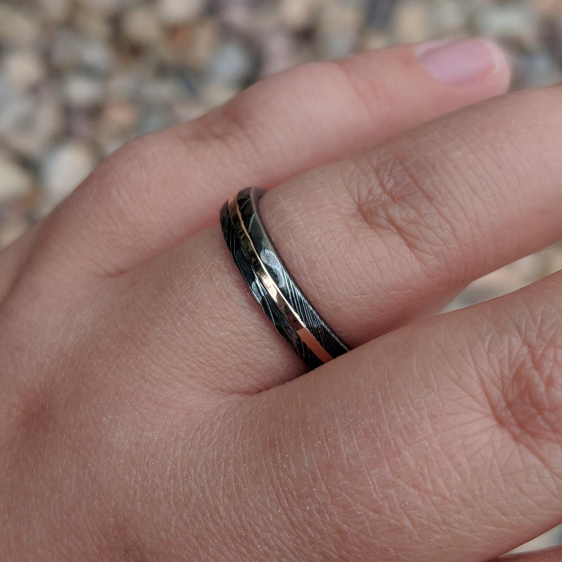 4mm wide Damascus steel ring with rose gold inlay and hammered finish on a finger