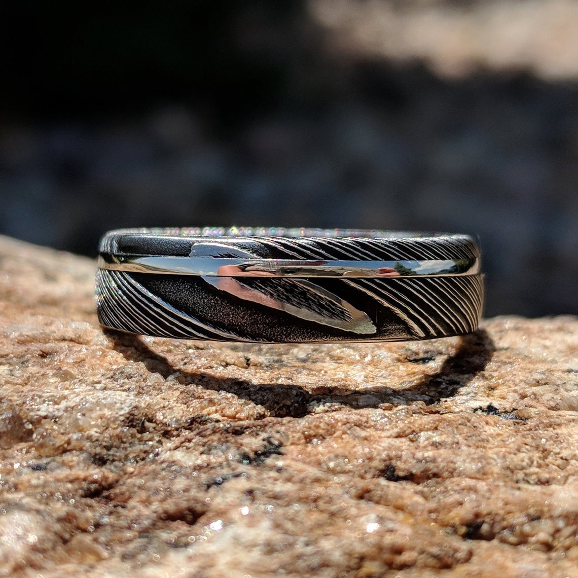 6mm wide black Damascus steel ring with an off-center white gold inlay