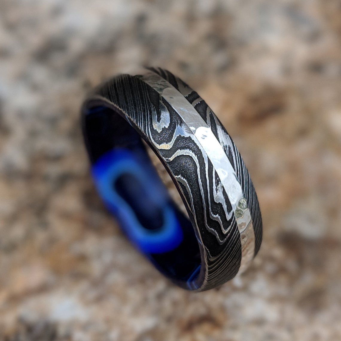 8mm wide black Damascus steel wedding band with a 2mm wide white gold inlay with a dark blue acrylic sleeve