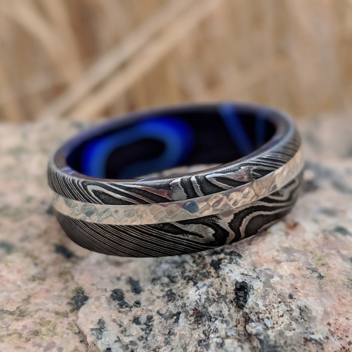 8mm wide black Damascus steel wedding band with a 2mm wide white gold inlay with a dark blue acrylic sleeve