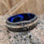 8mm wide black Damascus steel wedding band with a 2mm wide white gold inlay with a dark blue acrylic sleeve