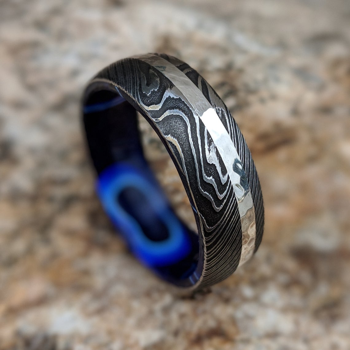 8mm wide black Damascus steel wedding band with a 2mm wide white gold inlay with a dark blue acrylic sleeve