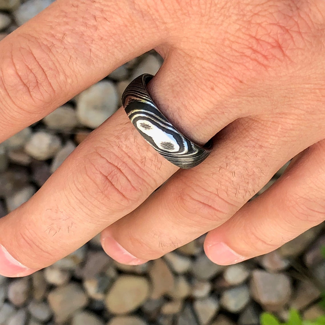 8mm wide Damascus steel wedding ring for men with a blue and black swirled cobaltium mokume sleeve on man&#39;s hand