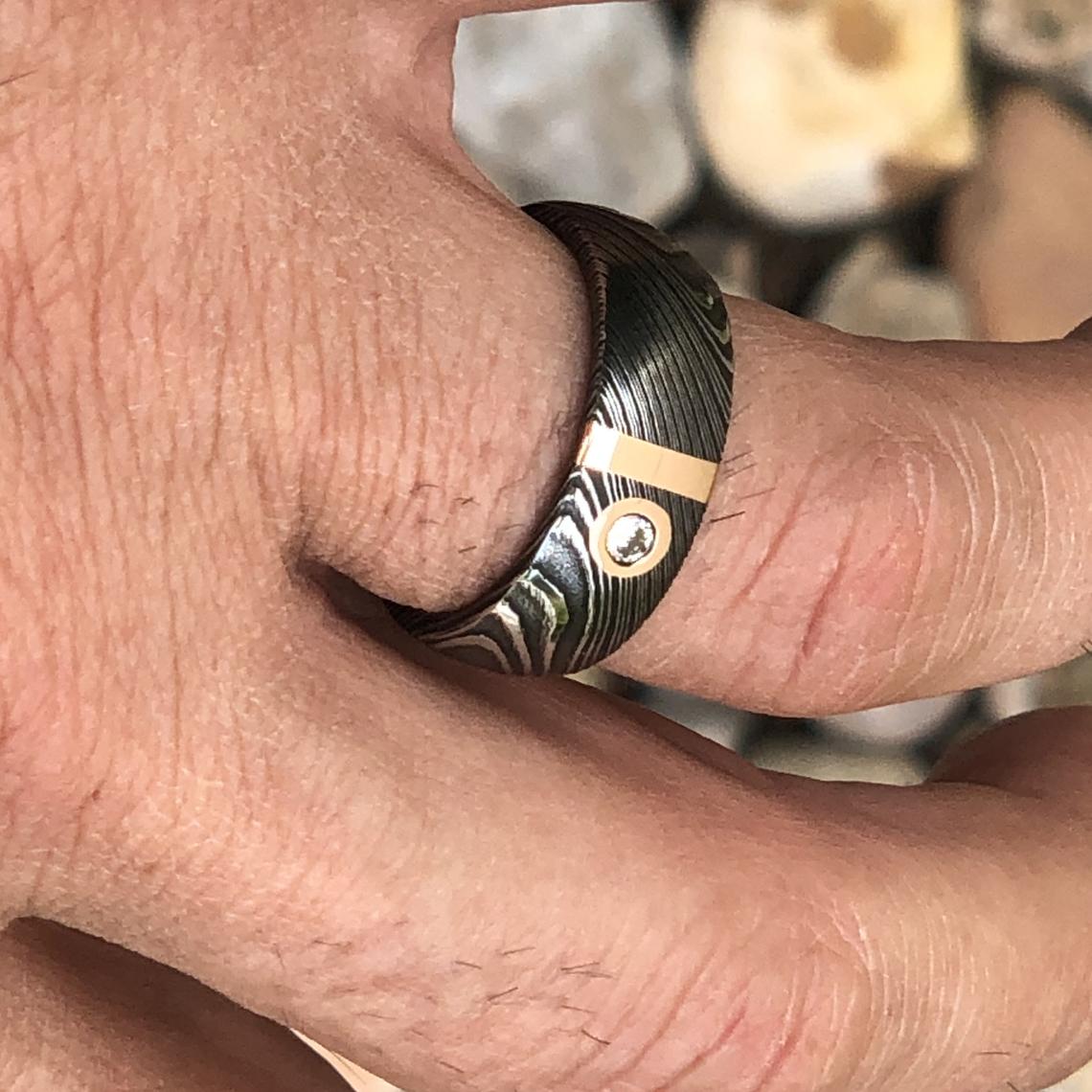 8mm wide black Damascus steel wedding band with 2mm wide gold inlay and a bezel set diamond