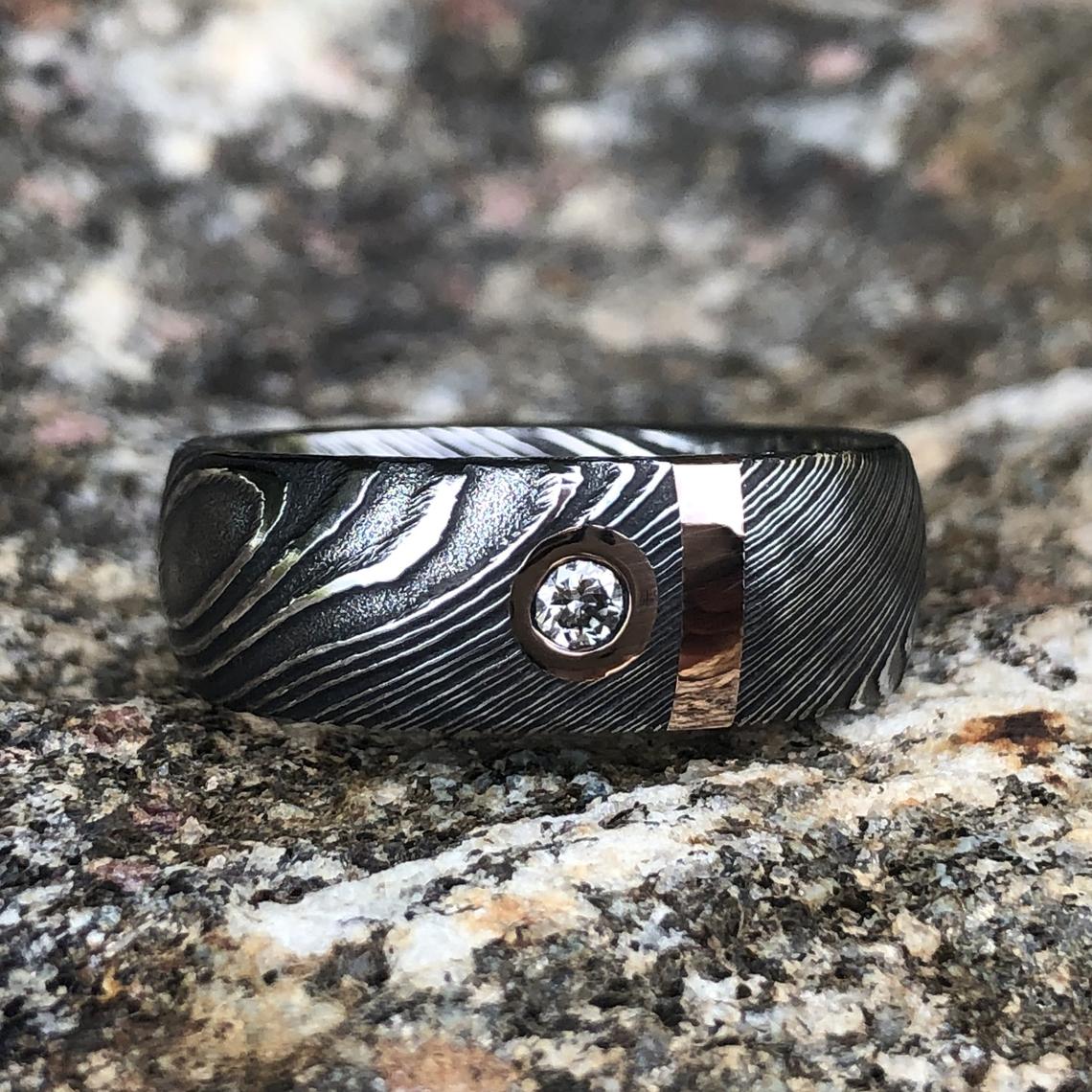 8mm wide black Damascus steel wedding band with 2mm wide gold inlay and a bezel set diamond