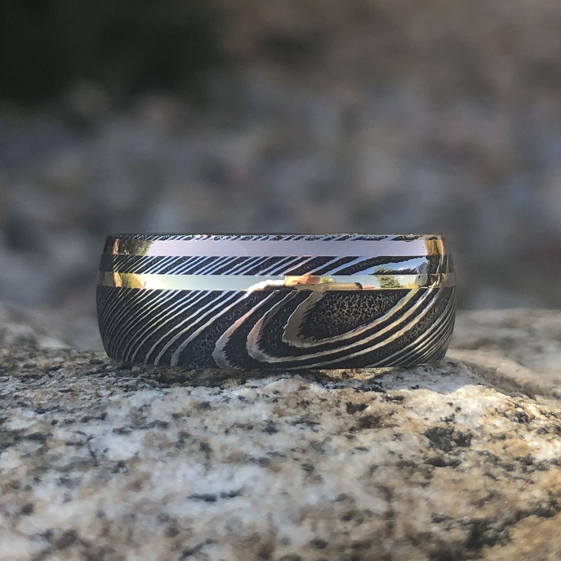 8mm wide black Damascus steel ring with dual inlay of rose gold and yellow gold with an Arizona ironwood sleeve