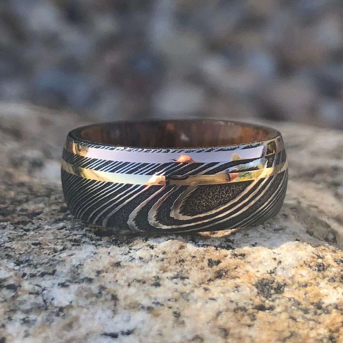 8mm wide black Damascus steel ring with dual inlay of rose gold and yellow gold with an Arizona ironwood sleeve