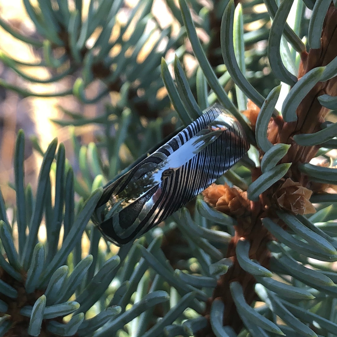 8mm wide black Damascus steel ring with an off-center white gold inlay and a green box elder sleeve