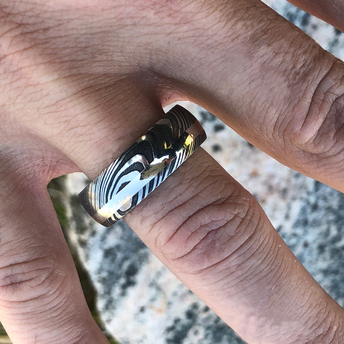 8mm wide black Damascus steel ring with an off-center white gold inlay and a green box elder sleeve on a man&#39;s hand