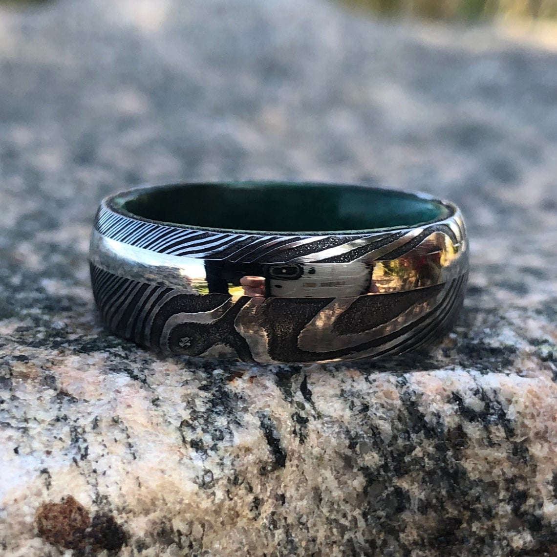 8mm wide black Damascus steel ring with an off-center white gold inlay and a green box elder sleeve
