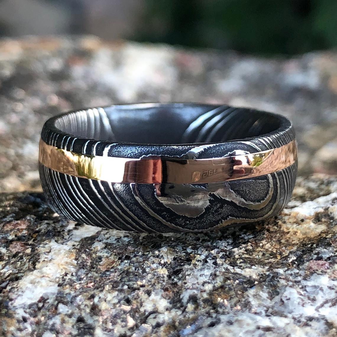 8mm wide black Damascus steel wedding band with a 2mm wide rose gold inlay and rounded profile