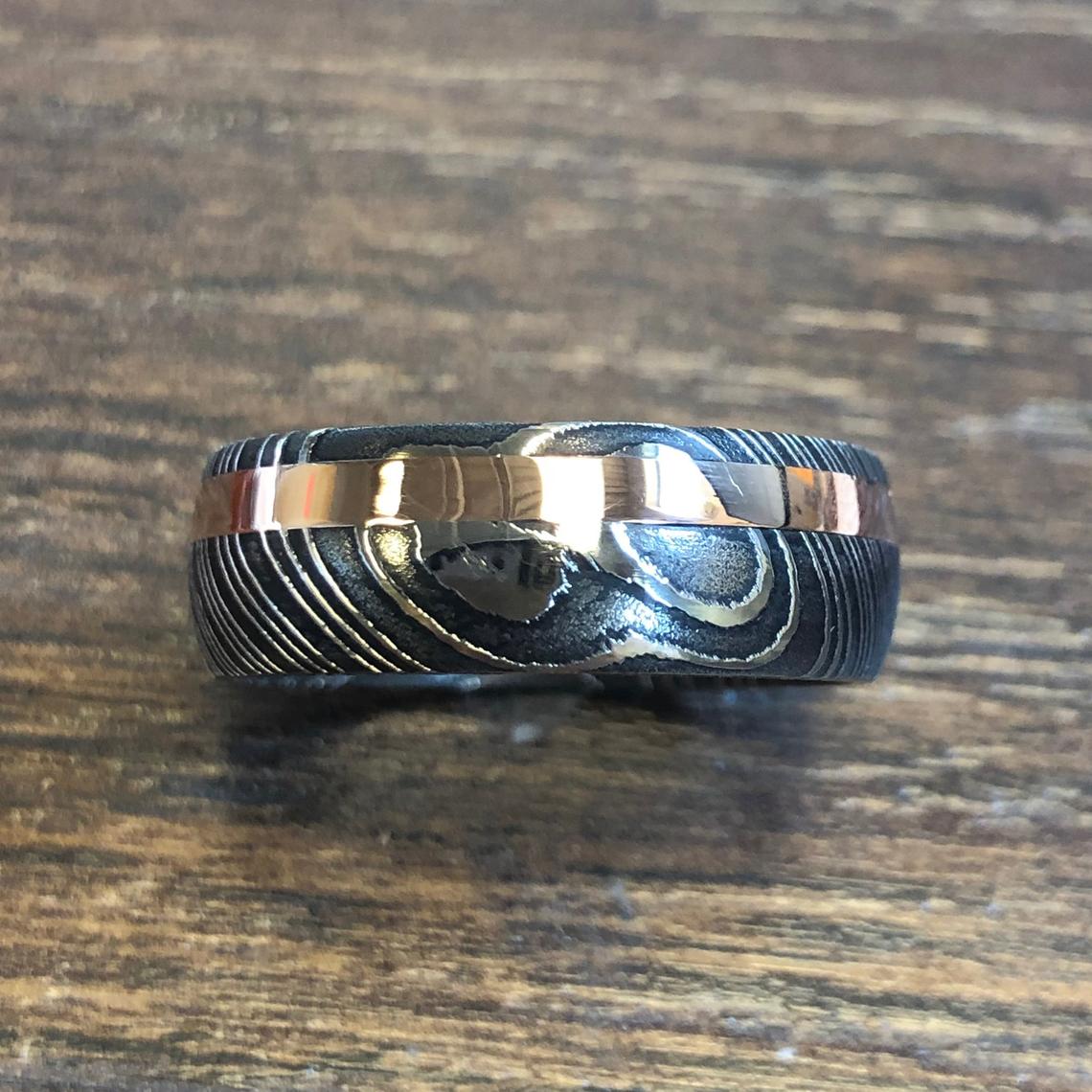 8mm wide black Damascus steel wedding band with a 2mm wide rose gold inlay and rounded profile