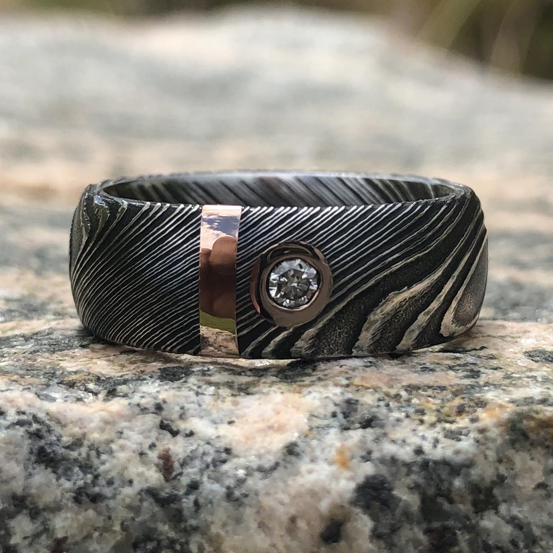 8mm wide black Damascus steel wedding band with 2mm wide gold inlay and a bezel set diamond
