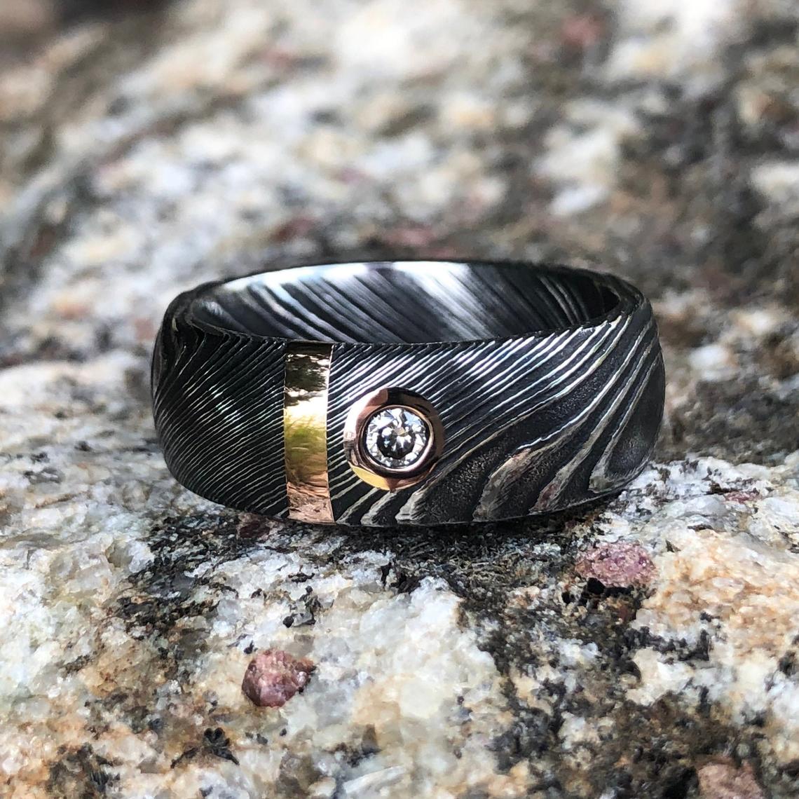 8mm wide black Damascus steel wedding band with 2mm wide gold inlay and a bezel set diamond
