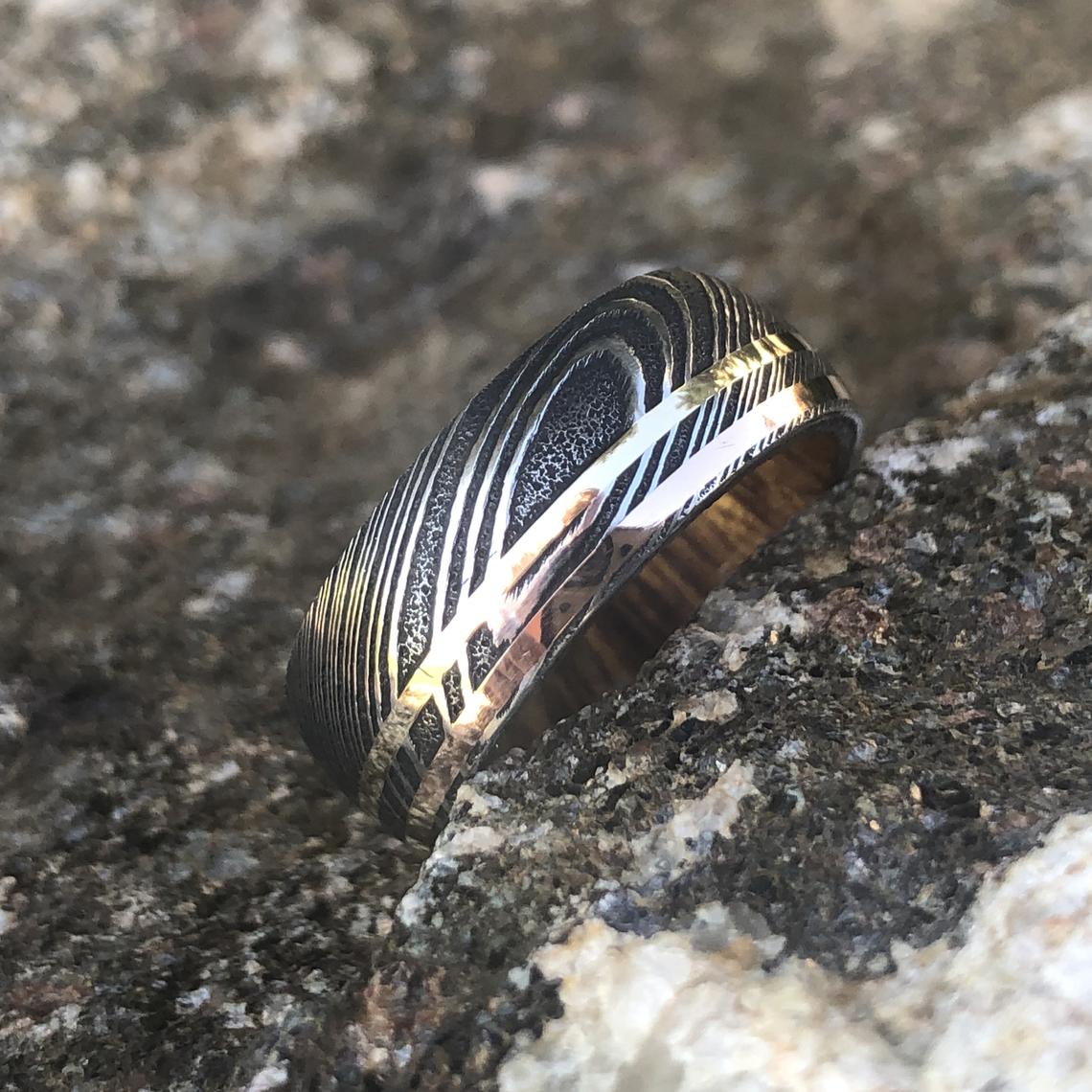 8mm wide black Damascus steel ring with dual inlay of rose gold and yellow gold with an Arizona ironwood sleeve