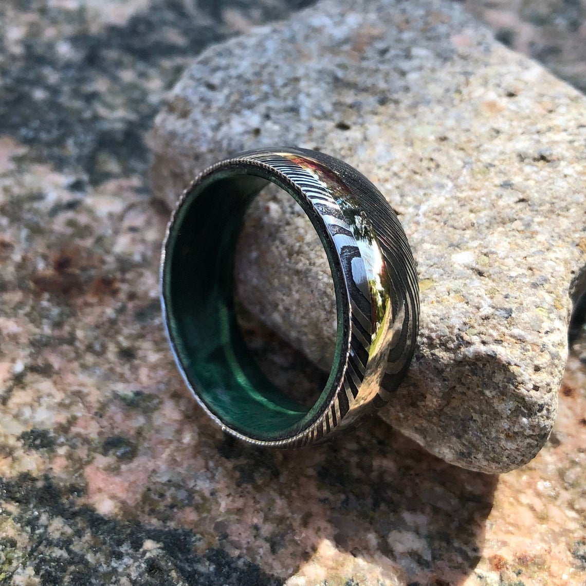 8mm wide black Damascus steel ring with an off-center white gold inlay and a green box elder sleeve