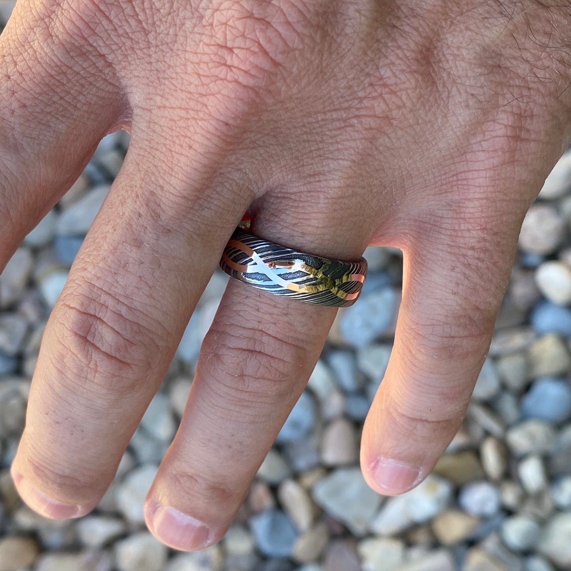 8mm wide Black Damascus steel ring with a 14k yellow gold infinity inlay on a man&#39;s hand