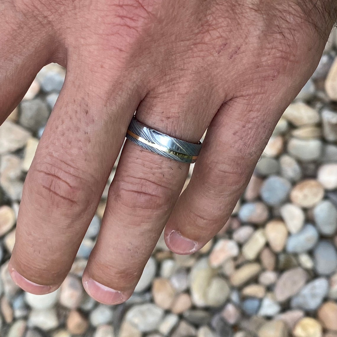 6mm wide white Damascus steel ring with a 14k yellow gold off-center inlay and sleeve on a man&#39;s hand