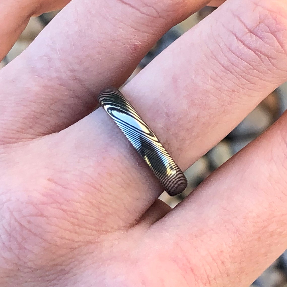 4mm wide Damascus steel wedding band with a rounded profile on a hand