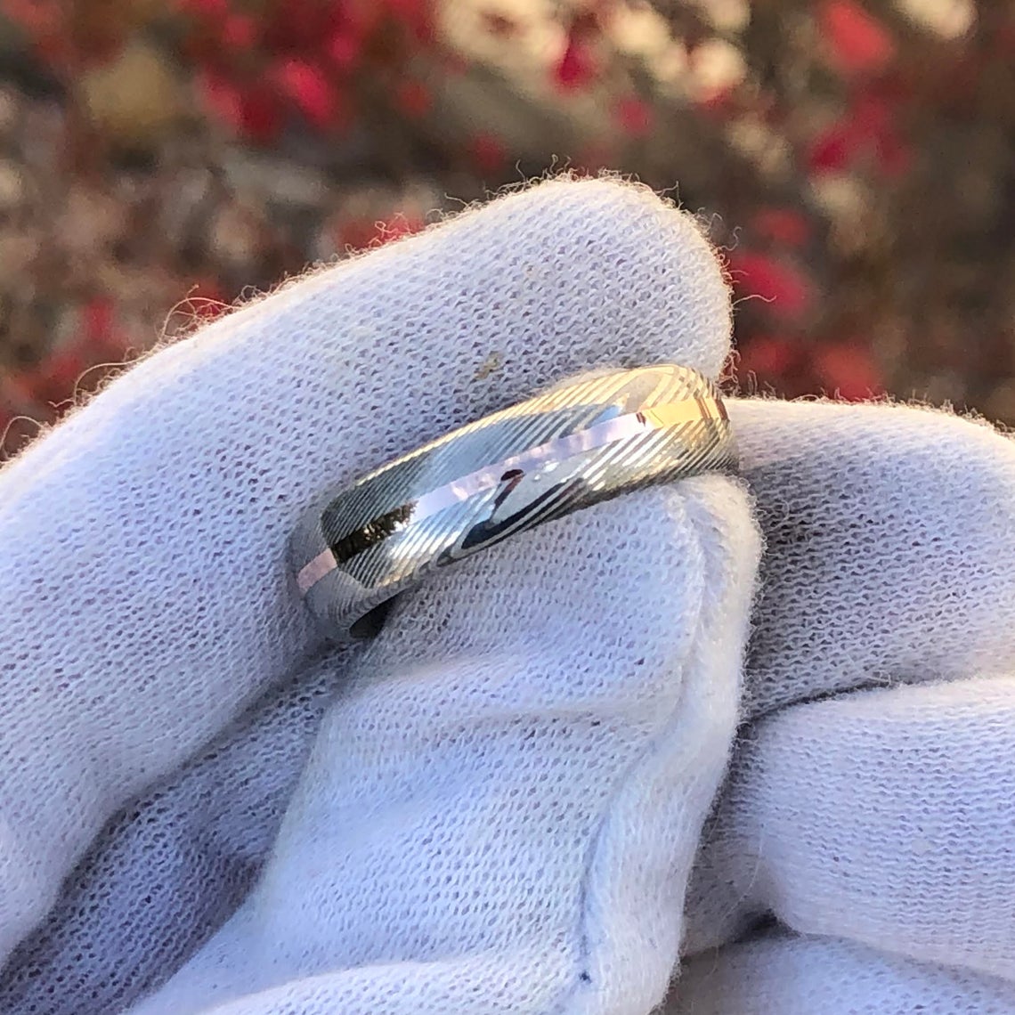 6mm wide Damascus steel wedding band with a centered rose gold inlay held by a white glove