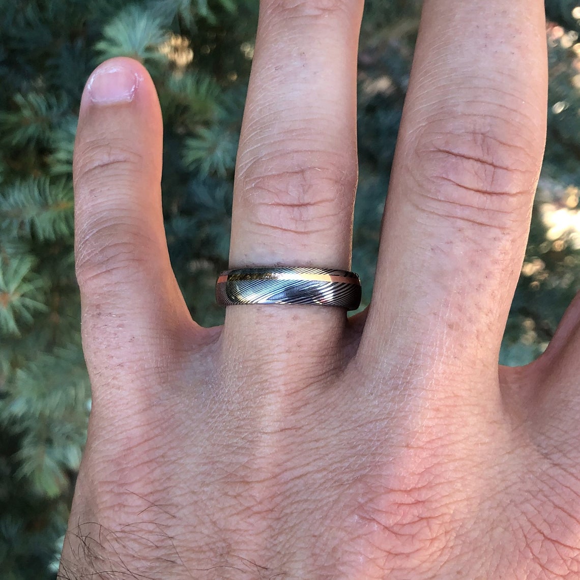 6mm wide Damascus steel ring with an off-centered rose gold inlay on man&#39;s hand