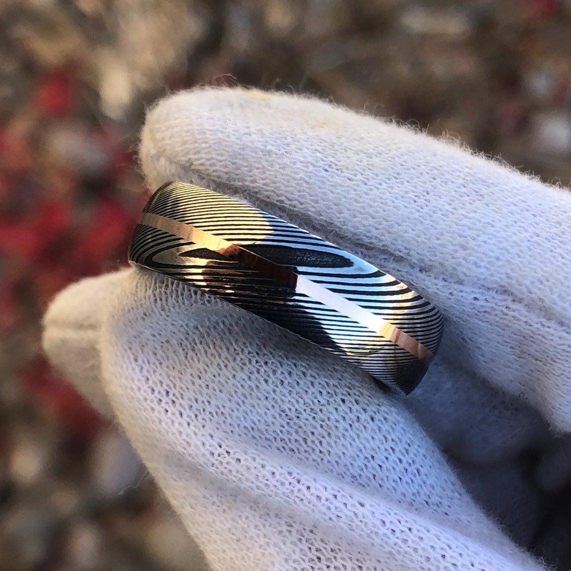 7mm wide Damascus steel ring with a centered rose gold inlay held by a white glove